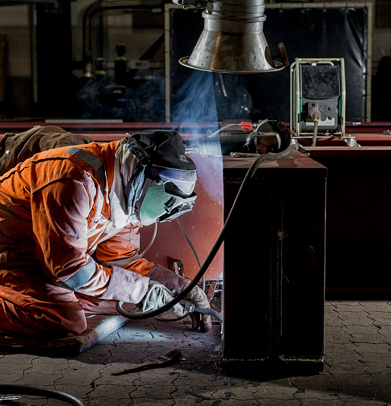 Welder crouching and welding a workpiece with Sigma in the background